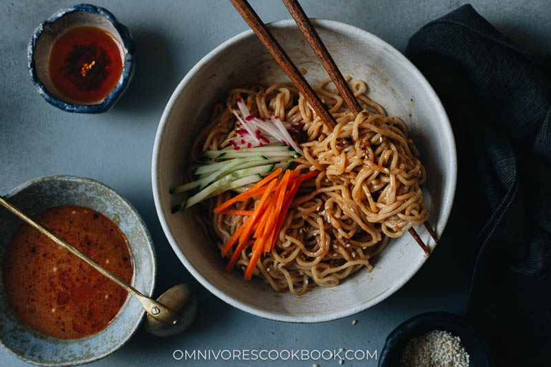 Bowls containing noodles, sauce, chili oil, and sesame seeds